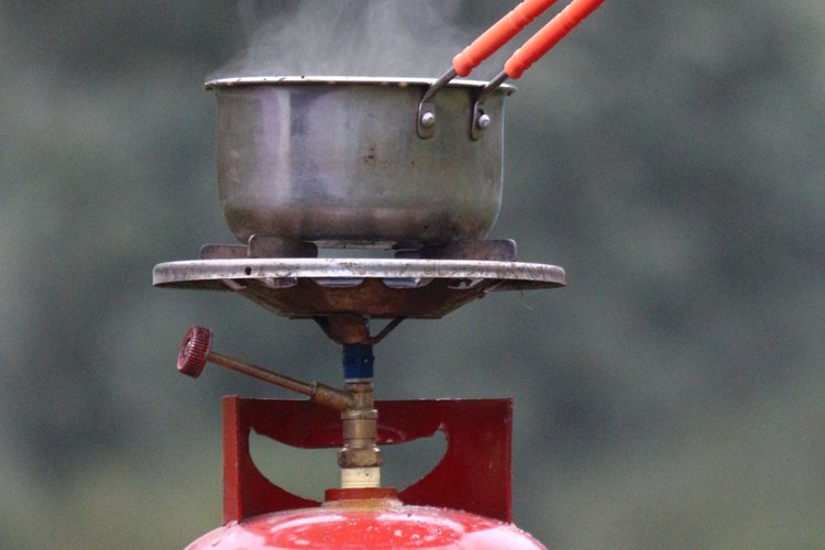 Panela a ferver ao ar livre sobre um queimador a gás montado numa garrafa vermelha